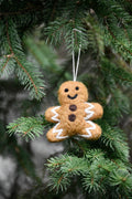 Bonhomme pain d'épices en feutre brun à décorations blanches sur une branche de sapin