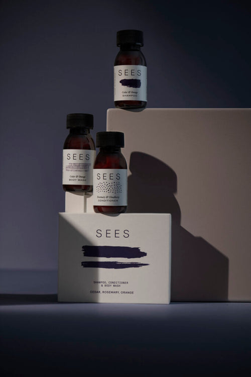 Kit de voyage SEES avec trois petits flacons de soin et leur emballage sur fond sombre